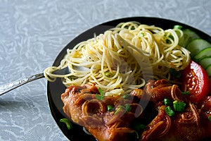 Un piatto con ali di pollo, spaghetti e pezzi di pomodori e cetrioli.