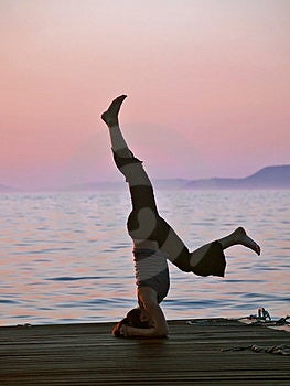 Mujer joven ejercicio, equilibrio sobre el cabeza, el mar a atardecer sobre el.