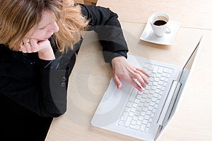 Obchodné žena v čiernom obleku pracovať na svojom notebooku s pol šálky kávy.