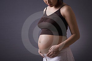 Studio záběr těhotná žena, která stála přes šedé pozadí s její žaludek vystaveny.