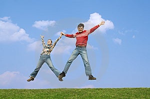 Dos joven saltando sobre el césped verde sobre el de oscuro cielo azul nubes.