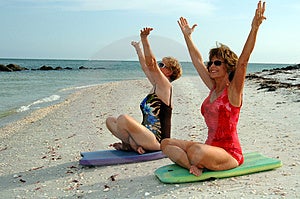 Due felici senior donna seduta su una spiaggia in una meditazione o di lode o di celebrazione di posa.