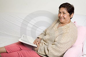 Senior asijské ženy relaxační doma na pohovce čtení knihy.
