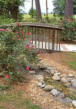 Dřevěné zdobené nohy mostu podél zahradní cesty přes růžovou zahradou.