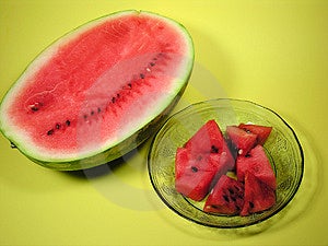 Jedna polovina velkého řez meloun vedle docela křišťálové misky s ovocem vzory vyryté do skla, naplněné čerstvé červené kousky melounu na žlutém pozadí.