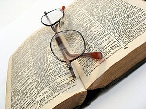 Libro aperto con gli occhiali su un semplice sfondo.