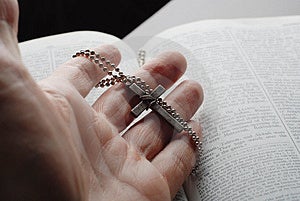 Bibliu otvorené s krížom v ruke.
