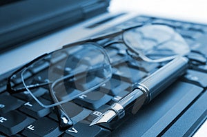 Eine Brille und einen Füllfederhalter auf einem laptop auf blau.