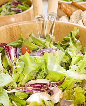 Zelený salát zblízka v dřevěné salátové mísy obsahující hlávkový salát, rukola (roket), čekanky (čekanka), cherry rajče, lněná a slunečnicová semínka.
