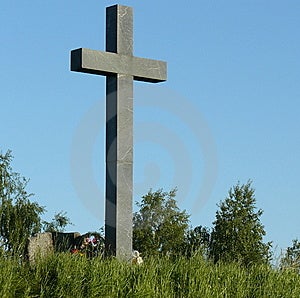 Ein graues Kreuz gegen den blauen Himmel.