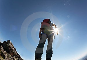 Bergsteiger, klettern, Gänge, stehend auf einem Stein an der Spitze seiner route, über einem tiefen blauen Himmel.