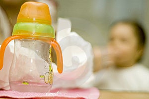 Dětská láhev s voda a neostré dítě v pozadí.