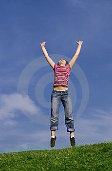Mladá šťastná žena skákat vysoko proti modré obloze.